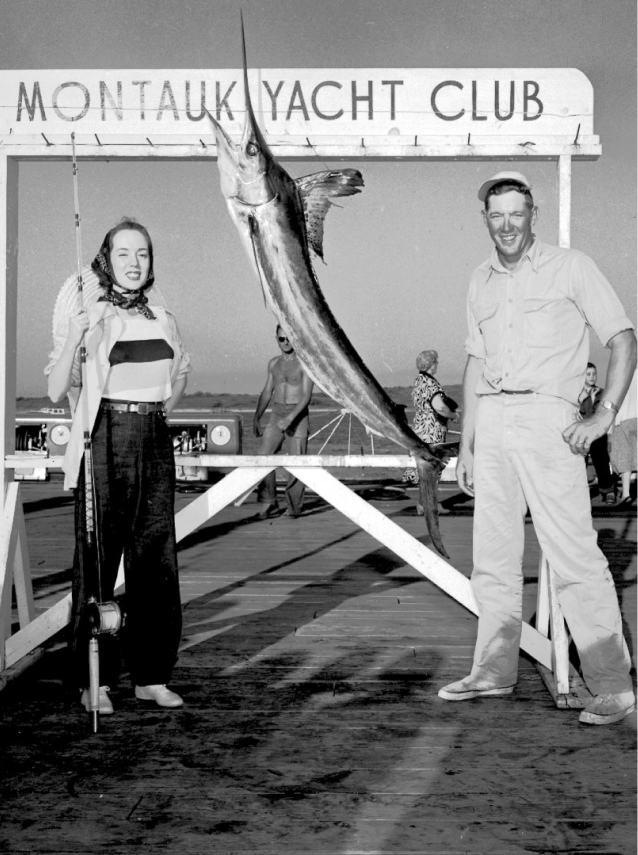 An old monochrome photo shows a man and a girl holding a big fish under a sign reading "MONTAUK YACHT CLUB".