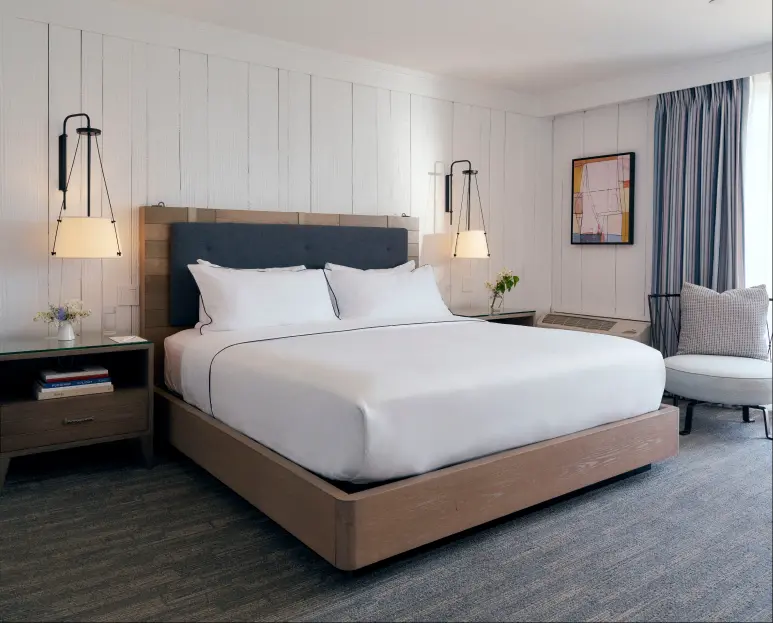 A well-arranged cozy bed with two lamps on either side and a portrait on the right wall.