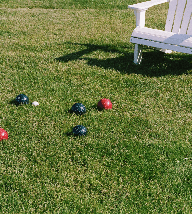 Bocce balls rest on the grassy ground near the bench.