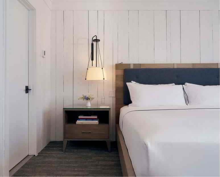 The cozy bed is well arranged with a side table and a glowing lamp above it.