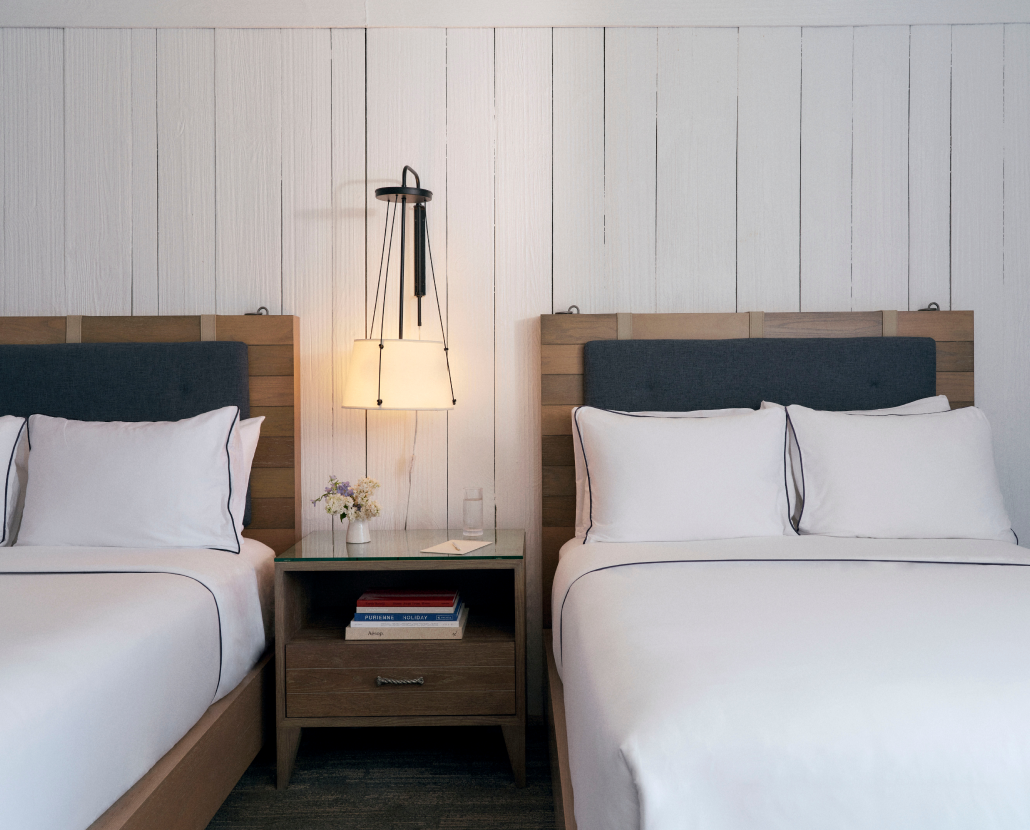 Two well-arranged cozy beds, separated by a side table with a glowing lamp mounted above it.