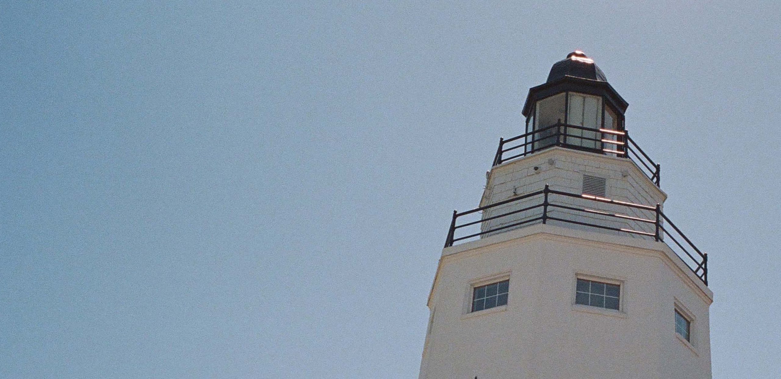 The top of a lighthouse shines brightly under the rays of the sun.