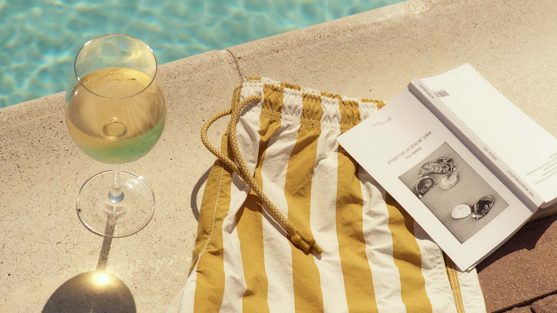 A boxer shorts, a notebook, and a wine glass are placed at the pool's edge.