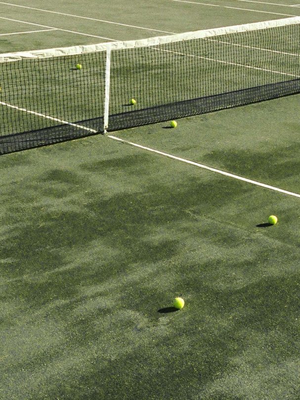 A tennis net and ball are set up on the grassy court for play.