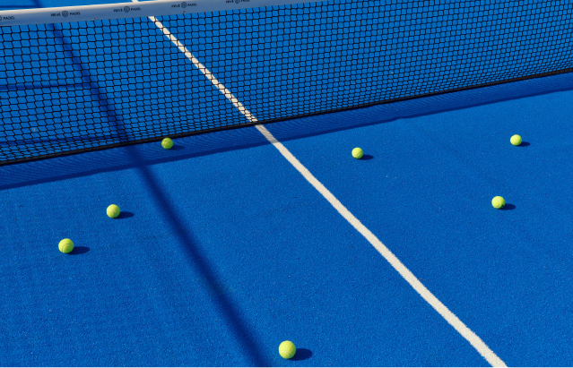 A tennis court with a net and tennis ball resting on the ground.