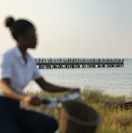 Staff member carrying basket near waterfront with wooden pier in background