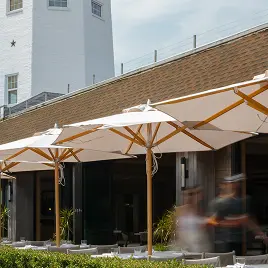 Outdoor patio seating with umbrellas beside building and lighthouse backdrop