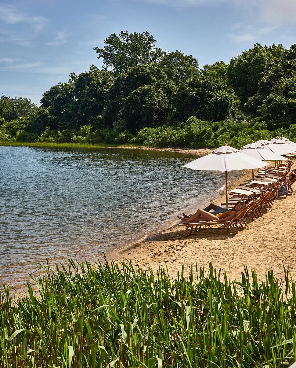 Person relaxing on a lounge chair under umbrella by lakeside beach