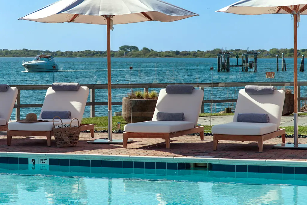 Poolside loungers with umbrellas overlooking waterfront and dock structures